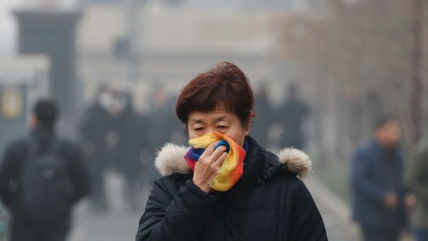 A woman uses a scarf to cover her for protection against air pollution walks on street in Beijing.