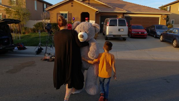 Neighbour Avery Sanchez, 6, walks with his mother Liza Tozier to drop off his large "Teddy" as a gift for the children who lived in the Turpin home.
