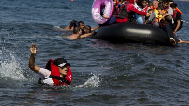 A Syrian man swims in front of a dinghy full of refugees. 