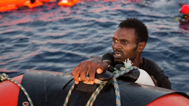 A refugee from Eritrea grabs a dinghy after jumping into the Mediterranean from a crowded wooden boat.