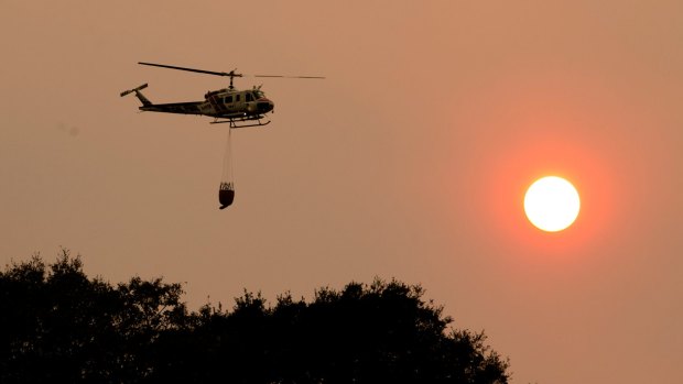 A helicopter flies through the smokey sky to drop a load of water on a wildfire in Sonoma, California.