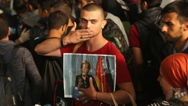 A migrant from Syria holds a picture of German Chancellor Angela Merkel as he and approximately 800 others arrive from Hungary at a Munich railway station.