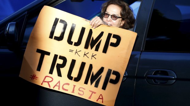 A woman holds a protest sign as she drives past the Luxe Hotel, where Republican presidential candidate Donald Trump was expected to speak in Brentwood, Los Angeles, California.