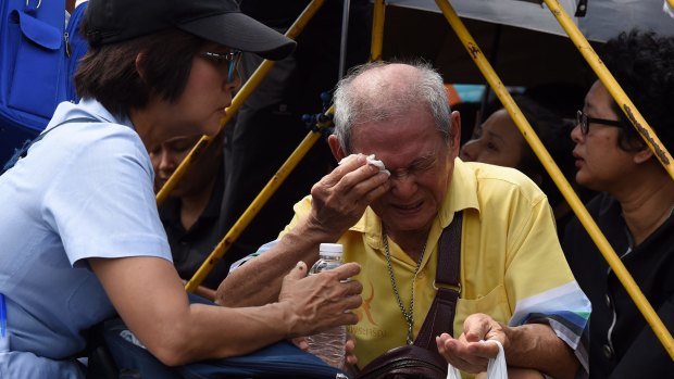 A man becomes ill and emotional outside the Grand Palace awating the king's body.