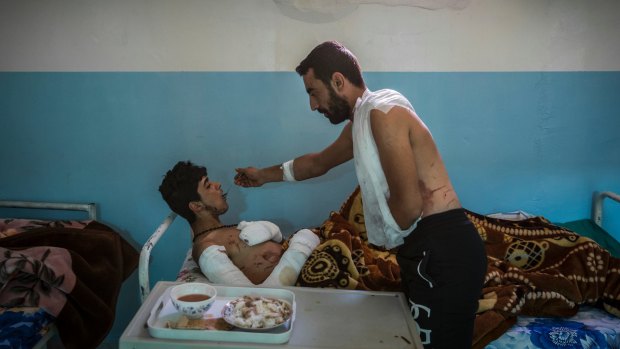 Mohammed Sheko feeds chicken and rice to his friend and fellow militiaman Salah al-Raqawi, as they both recuperate from injuries suffered ousting Islamic State militants from Raqqa.