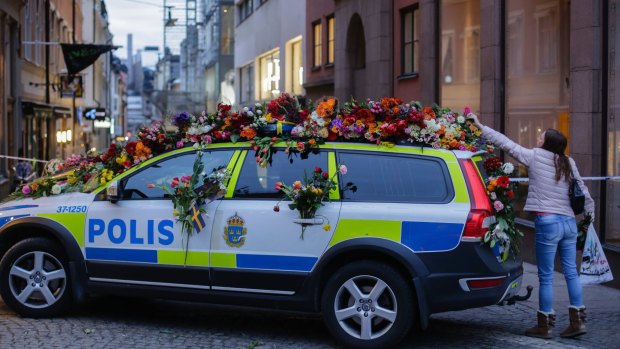 A woman drops flowers onto a police car near the department store Ahlens following a suspected terror attack in central Stockholm.
