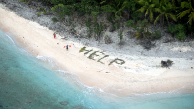 Two men wave lifejackets beside the word "help" spelled out in palm leaves on the beach on the uninhabited island of Fanadik.