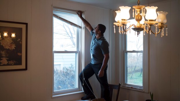 Luis Manuel Ortiz, a case worker with the Church World Service, hangs blinds in the home being prepared for the arrival of a Syrian refugee family.