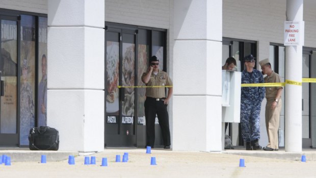 Reserve Recruitment personnel stand outside a Navy recruiting building as the area is cordoned off with blue shell casing markers.