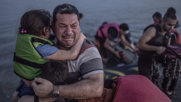 A Syrian refugee from Deir Ezzor, holding his son and daughter, breaks out in tears of joy after arriving via a flimsy inflatable boat crammed with about 15 men, women and children on the shore of the island of Kos in Greece.