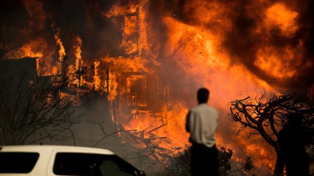 A man watches flames consume a residence as a wildfire rages in Ventura, California.