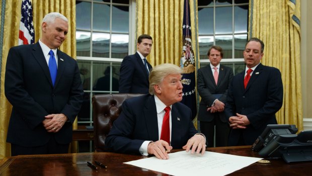 Vice President Mike Pence watches at left as President Donald Trump prepares to sign his first executive order in the Oval Office of the White House in Washington.