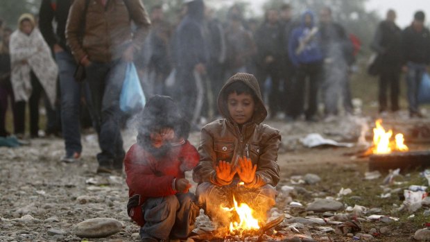 Two boys warm themselves by a fire while other migrants and refugees walk towards the transit camp for refugees near the southern Macedonian town of Gevgelija after crossing the border from Greece. 