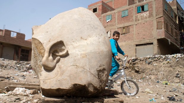 A boy rides his his bicycle past a recently discovered statue in a Cairo slum of pharaoh Ramses II.