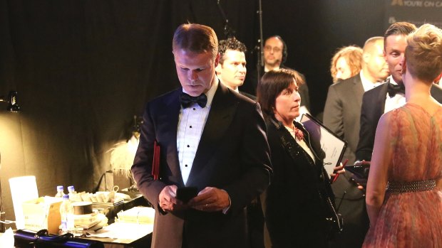 Brian Cullinan, centre, holds red envelopes under his arm while using his phone backstage at the Oscars.