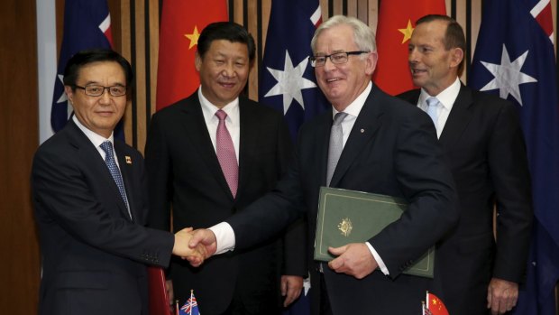 Chinese President Xi Jinping and Prime Minister Tony Abbott watch as Trade Minister Andrew Robb and Chinese Commerce Minister Gao Hucheng shake hands.