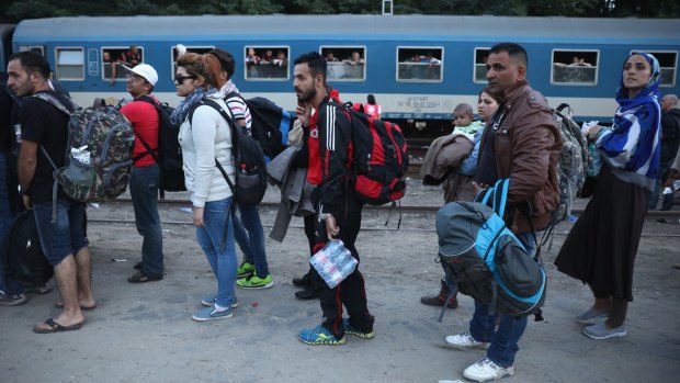 People queue as hundreds of refugees pack onto a train at Roszke train station destined for the Austrian border, after the Hungarian authorities closed the open railway track crossing.