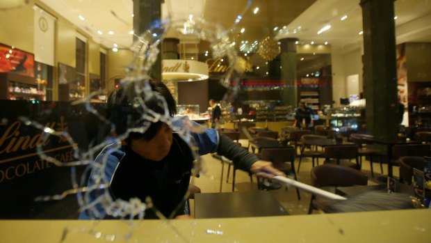 A man cleans up broken glass from vandalised windows at the Lindt cafe in Martin Place, Sydney.