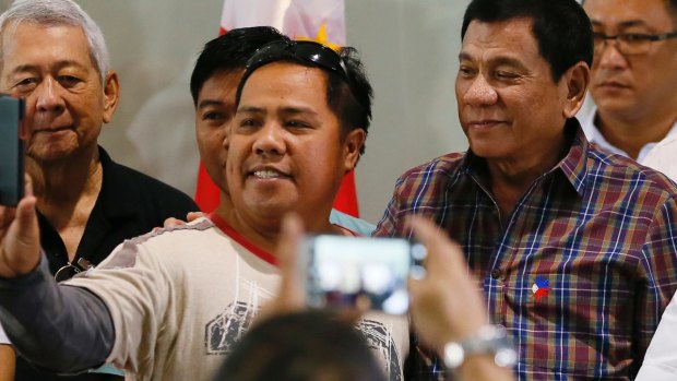 Philippine President Rodrigo Duterte, right, poses for a selfie with a returning Filipino worker.