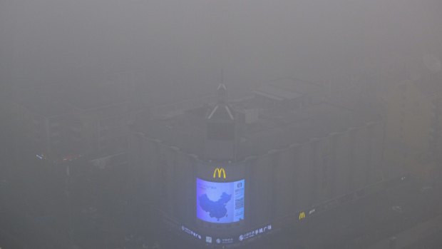 A video display on the side of a building shows a map of China amid heavy pollution and fog in Beijing.