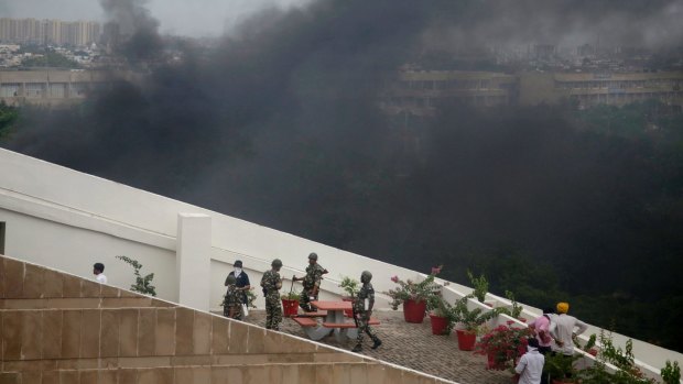 Black smoke rises in the background as Indian security officers take shelter on the roof of a government building after Dera Sacha Sauda sect members went on a rampage in Panchkula, India.