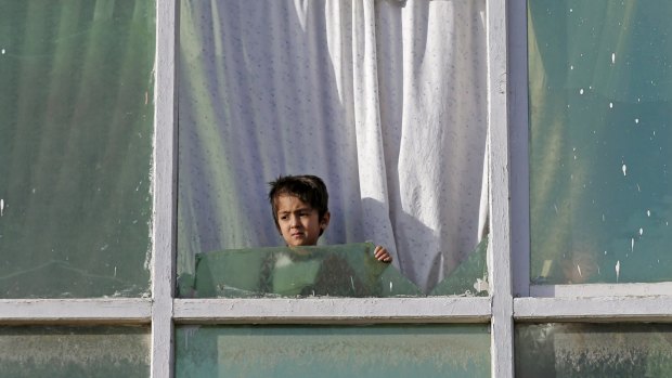 An Afghan child boy looks out from the broken window of a house near the site of a bomb attack.
