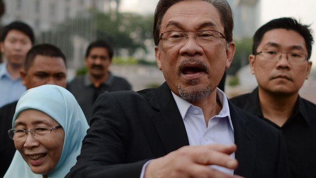 Malaysian Opposition leader Anwar Ibrahim (centre) gestures as he walk with his wife Wan Azizah (left) towards his supporters before entering the court. 