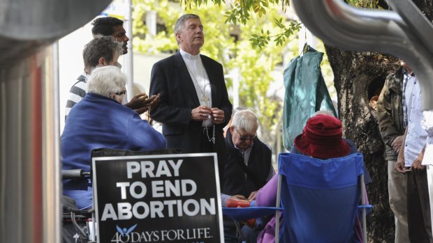 Vigil: The Roman Catholic Archbishop of Canberra and Goulburn, Christopher Prowse, centre, joins others in prayer outside the ACT Health building in Moore Street, Civic.