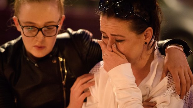 A woman is consoled as she looks at the floral tributes following an evening vigil outside the Town Hall in Manchester, England.