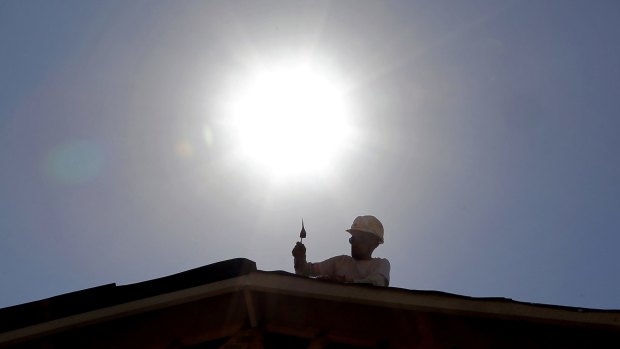 A roof repairer works under the midday sun in Gilbert, Arizona.
