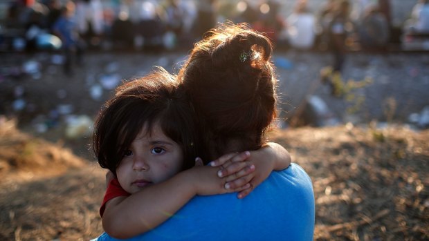 A young Syrian migrant girl is held by her mother next to railroad tracks where migrants wait to cross into Macedonia in Idomeni, Greece. 