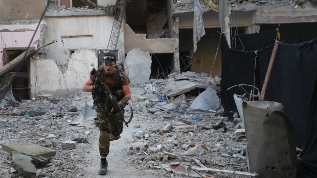 A US-backed Syrian Democratic Forces fighter runs in front of a damaged building as he crosses a street on the front line, in Raqqa, Syria in July.