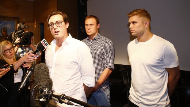 Nick Kelly, one of the nine Australians who stripped at the Formula One in Malaysia last weekend, delivers a statement at Sydney International Airport on their return. Behind him are Thomas Laslett and Edward Leaney, right.
