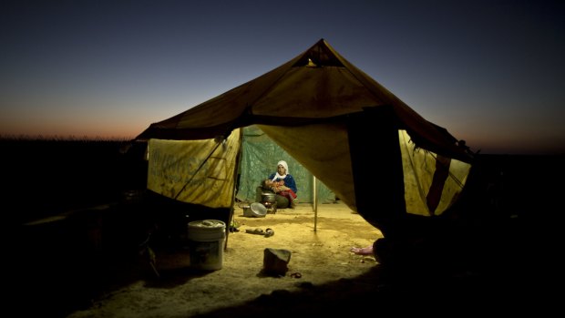 A Syrian refugee tends to her daughter while cooking inside her tent at an informal tented settlement near the Syrian border on the outskirts of Mafraq, Jordan.