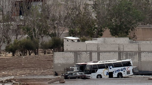 An alleged Islamic State militant (to the left of buses) takes cover behind a wall in the Syrian town of Kobane on Wednesday.