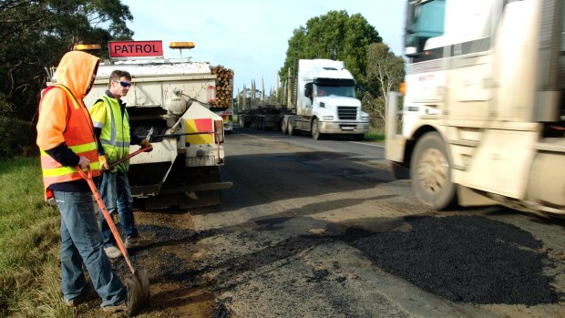 Road workers try to patch a pothole on the Henty Highway near Portland as trucks thunder past.