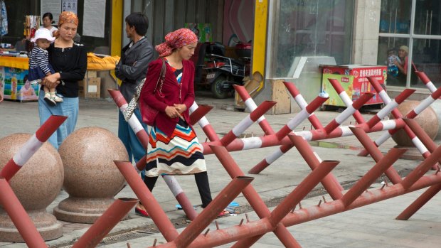 Clampdown: Uighur women walk past barricades at the entrance to a shopping district in Aksu in western China's Xinjiang province.