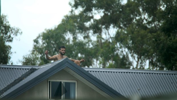 A man sits on the roof of a townhouse in Tighes Hill, as police attempt to negotiate with him.