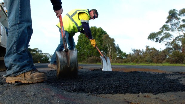 Workmen shovel asphalt into holes on the Henty Highway near Portland.
