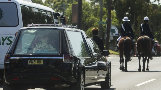 A pair of mounted police lead the hearse away.