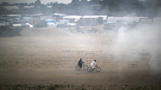 Migrants cycle through smoke on the outskirts of the Calais 'Jungle' camp.