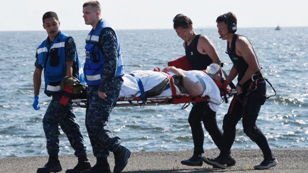 An injured US Navy sailor is carried by US military personnel (left) and Japanese Maritime Self-Defense Force members.