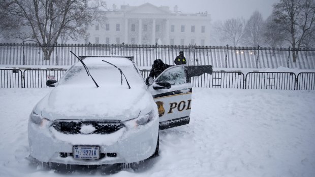 A uniformed Secret Service officer opens a car door on a patrol car that was frozen shut during blizzard conditions.