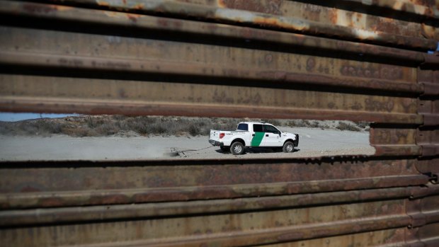 A Border Patrol vehicle drives by in Tecate, California, seen through a hole in the metal barrier that lines the border.