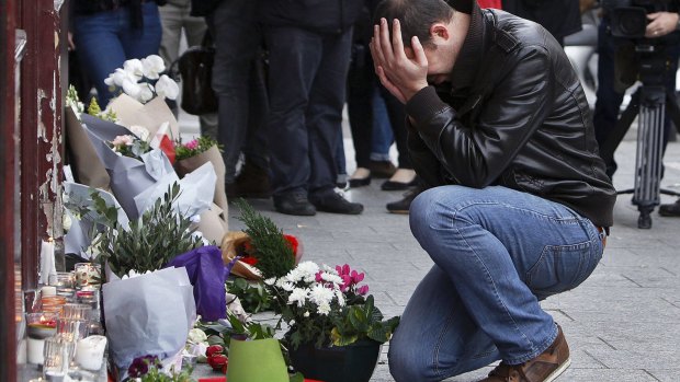 Grief stricken: A man lays flowers at the scene of one of the attacks, in front of the Carillon cafe, in Paris. 