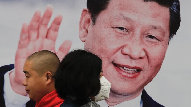 A masked woman and a man walk by a poster of Chinese President Xi Jinping on a street in Beijing.