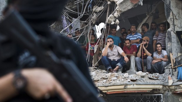Defiant parade: Palestinians sit in the rubble of a building as they watch Hamas militants parade their weapons.