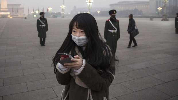 A Chinese woman looks at her phone as Chinese Paramilitary police wear masks to protect against pollution as they stand guard during smog in Tiananmen Square.