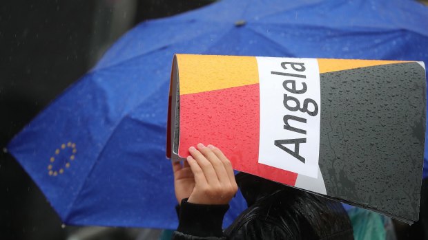A supporter uses a sign to shield the rain during an election campaign rally for Angela Merkel.