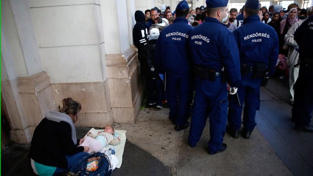 A Syrian woman changes her baby's diaper next to a line of Hungarian police at Keleti train station.